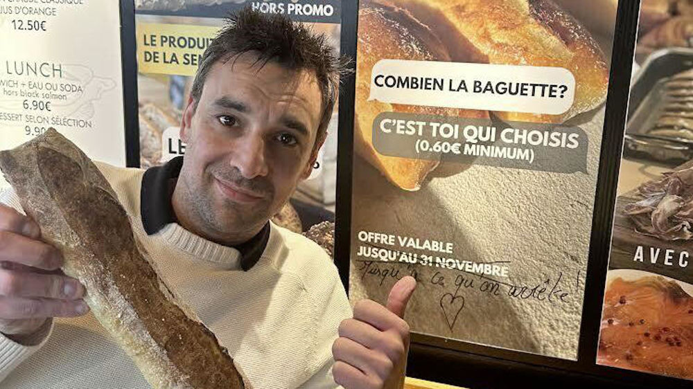 Pour la Toque, Maxime Lefebvre pose devant une affiche de son opération Baguette à prix libre.