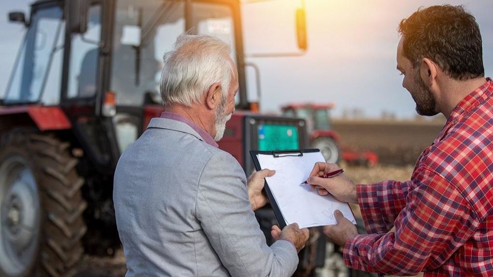 Vieil et jeune agriculteur devant un tracteur
